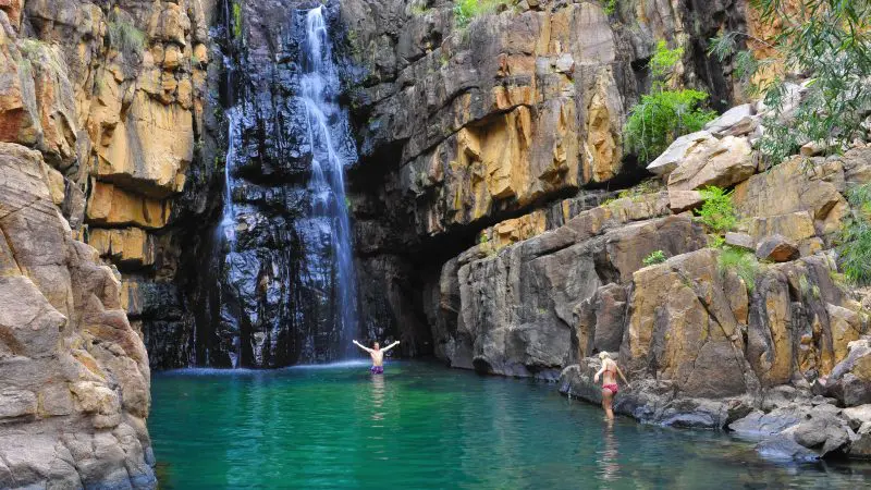 Two adventurers swim by a scenic waterfall during a 5 Day Kakadu, Katherine Gorge, and Litchfield 4WD tour from Darwin.