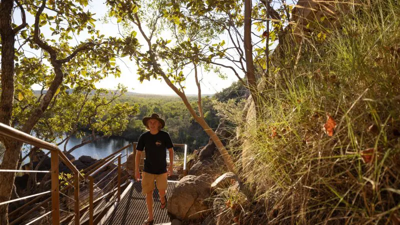 Traveller in a wide-brimmed hat ascends a metal stairway amid lush greenery on the 4 Day Kakadu Katherine Gorge Adventure from Darwin.