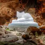 Breathtaking panoramic view from inside a rugged cave on the 3 Day Great Ocean Road Melbourne to Adelaide tour, overlooking lush green countryside.