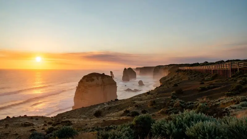 Breathtaking sunset illuminates limestone stacks and a scenic boardwalk at the Twelve Apostles on the Great Ocean Road, Adelaide to Melbourne.