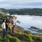 Three travellers on a lush hill enjoy the 3 Day Great Ocean Road & Grampians Explorer tour, returning to Melbourne’s stunning views.