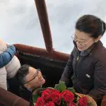 Romantic hot air balloon proposal over Melbourne City, man holding red roses above clouds with skyline views in breathtaking sunrise.