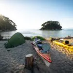 Kayaks and a green tent rest on a pristine sandy beach beside tranquil waters and scenic islands—ideal for a Three Day Classic adventure.