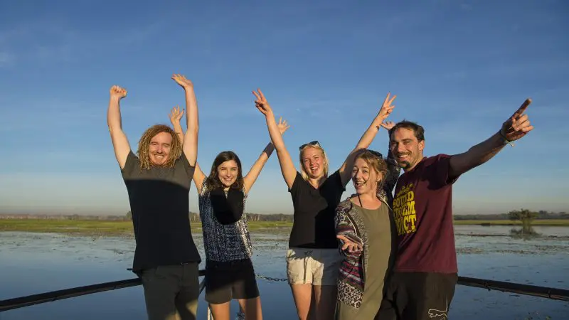 Group of five people celebrating on a boat, taking in Kakadu and Litchfield National Park’s stunning landscapes on a 3-day 4WD safari tour.
