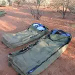Two green camping swags with bedding on rich red earth, ideal accommodation for a 2 Day Uluru Kata Tjuta Rock Tour from Ayers Rock.