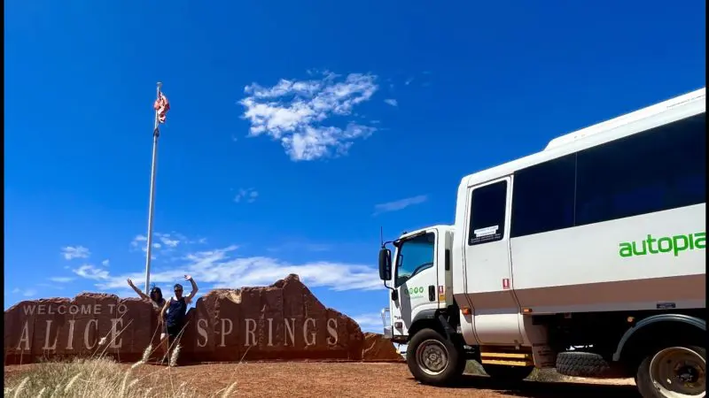 Three travellers stand by the Welcome to Alice Springs sign before starting their epic 3-Day Red Centre Uluru Kings Canyon Safari tour.