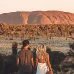A couple admires Uluru glowing at sunset during a guided 4-day Uluru, Kata Tjuta, Kings Canyon & West MacDonnell desert tour.