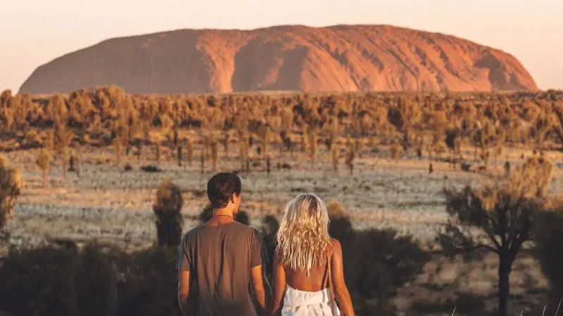 Couple enjoys vibrant sunset over Uluru and Kata Tjuta on a 2-day outback tour from Ayers Rock Yulara, stunning desert views.