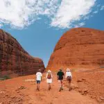 Visitors hike between stunning red rock formations under a clear sky on a 2 Day Uluru Kata Tjuta Tour departing from Ayers Rock Yulara.