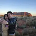 Couple capture a sunset selfie at Uluru on their 4-Day Uluru Kata Tjuta Kings Canyon tour, highlighting iconic Australian outback.