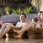 Group of four adults and a baby enjoy relaxing outdoor hot tubs at Peninsula Hot Springs after a one-day spa entry shuttle bus experience.