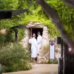 Two guests in white dressing gowns enter a luxurious stone sauna at Peninsula Hot Springs after arriving via the 1 Day Spa Entry Shuttle Bus.