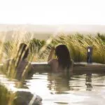 Two people relax in an outdoor hot tub at sunset after a 1 Day Peninsula Hot Springs Spa Entry tour, enjoying luxury and stunning views.
