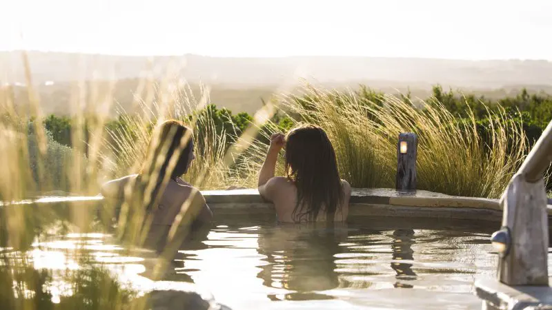 Two people relax in an outdoor hot tub at sunset after a 1 Day Peninsula Hot Springs Spa Entry tour, enjoying luxury and stunning views.