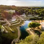 Aerial view of lush park with winding path, serene pond, leafy trees, and visitors—ideal prelude to your Peninsula Hot Springs Spa shuttle.