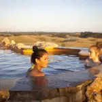 Two women unwind in a scenic hot spring pool at sunset, experiencing 1 Day Peninsula Hot Springs Spa Entry Coach relaxation.