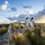 Two women in white robes relax at sunset near their Peninsula Hot Springs Spa Shuttle Bus, capturing a tranquil wellness retreat moment.