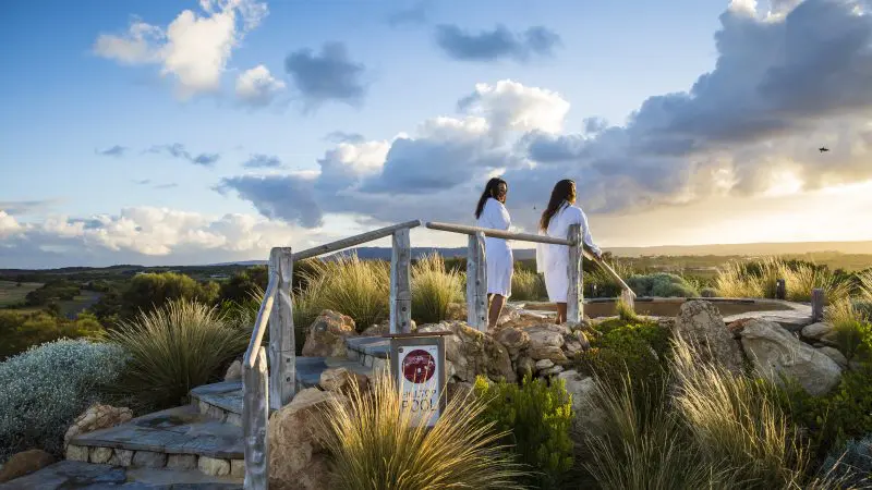 Two women in white spa robes relax at sunset after a 1 Day Peninsula Hot Springs Spa Entry Shuttle Bus experience, serene backdrop.