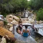 Visitors unwind in scenic outdoor Peninsula hot springs after convenient shuttle bus arrival with 1 Day Spa Entry, enjoying relaxation.