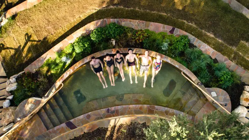 A group of six people in swimsuits unwind together at Peninsula Hot Springs, making the most of a 1 Day Spa Entry with Shuttle Bus.