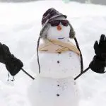 Cheerful snowman with sunglasses, checked hat, and scarf welcomes you to the 1 Day Lake Mountain Snow Waterfalls Tour from Melbourne.