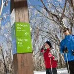 Two travellers in winter gear study trail signs on the snowy Lake Mountain Snow Waterfalls day tour departing from Melbourne.