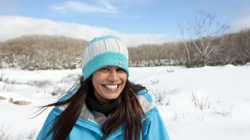 Happy woman in blue jacket and beanie enjoys scenic snowy landscape on Lake Mountain Snow Waterfalls Day Tour from Melbourne.