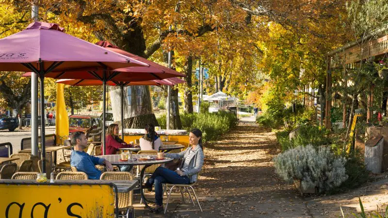 Visitors relax at outdoor café tables beneath vibrant red umbrellas, enjoying a break before a 1 Day Lake Mountain Snow Tour from Melbourne.