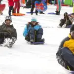 Tourists toboggan down a snowy hill at Lake Mountain on a 1 Day Snow Waterfalls Tour from Melbourne, experiencing winter adventure.