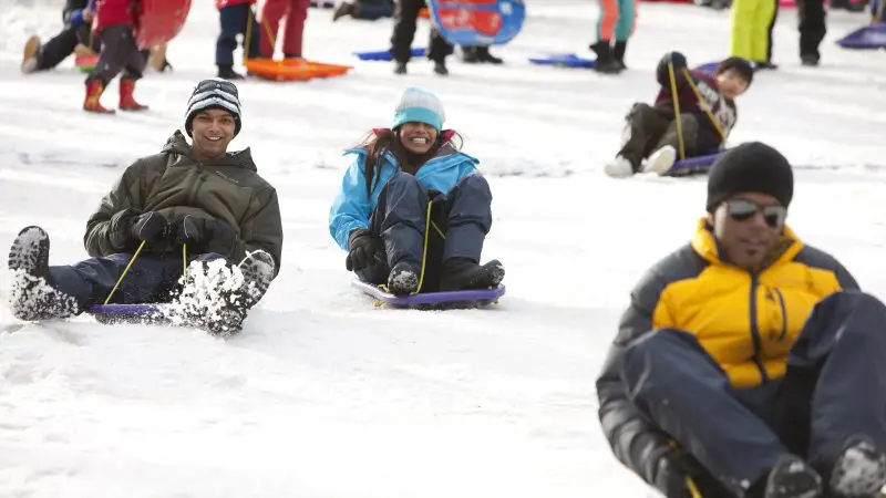 Tourists toboggan down a snowy hill at Lake Mountain on a 1 Day Snow Waterfalls Tour from Melbourne, experiencing winter adventure.