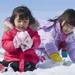 Children in colourful winter coats play joyfully in fresh snow, capturing the fun of a Lake Mountain Snow Tour near Melbourne.