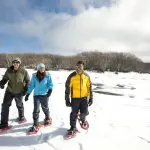 Three adventurers in winter gear snowshoe across snowy Lake Mountain, the ideal spot for a 1 Day Lake Mountain Snow Tour from Melbourne.