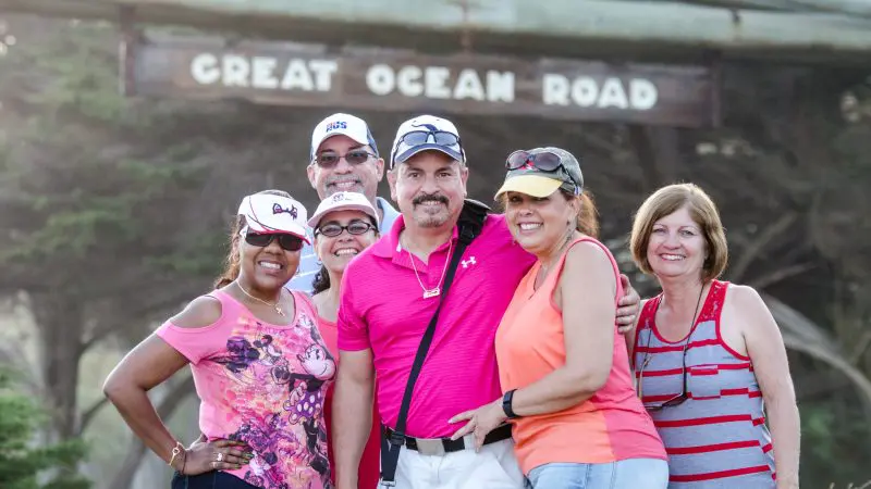 Group of six happy adults pose by the iconic Great Ocean Road sign on a 1 Day Reverse Eco Tour, enjoying scenic Australian adventure.