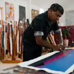 Artist painting a vivid abstract, with 7 Day Adelaide to Uluru Adventure Untamed Escapes brochures prominently displayed nearby.