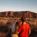 Couple gazes at Uluru during a stunning sunset on a 7-day Adelaide to Uluru Adventure by Untamed Escapes, Australia tour.