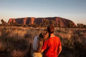 A couple stands before Uluru at sunset during a breathtaking 7 Day Adelaide to Uluru Adventure by Untamed Escapes tour.