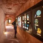 A woman explores a tunnel-shaped museum corridor with opal displays during the 7 Day Adelaide to Uluru Adventure by Untamed Escapes.