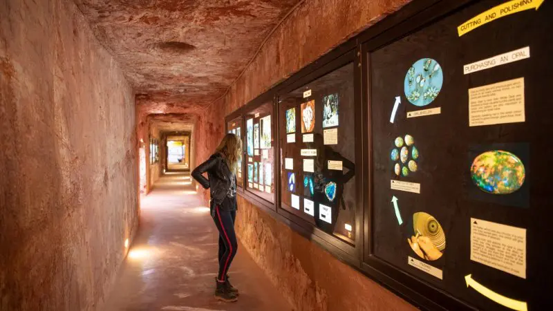 A woman explores a tunnel-shaped museum corridor with opal displays during the 7 Day Adelaide to Uluru Adventure by Untamed Escapes.