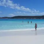 Woman on pristine white sand during 10 Day Perth to Adelaide Adventure Tour by Untamed Escapes; others enjoy crystal-clear blue water.