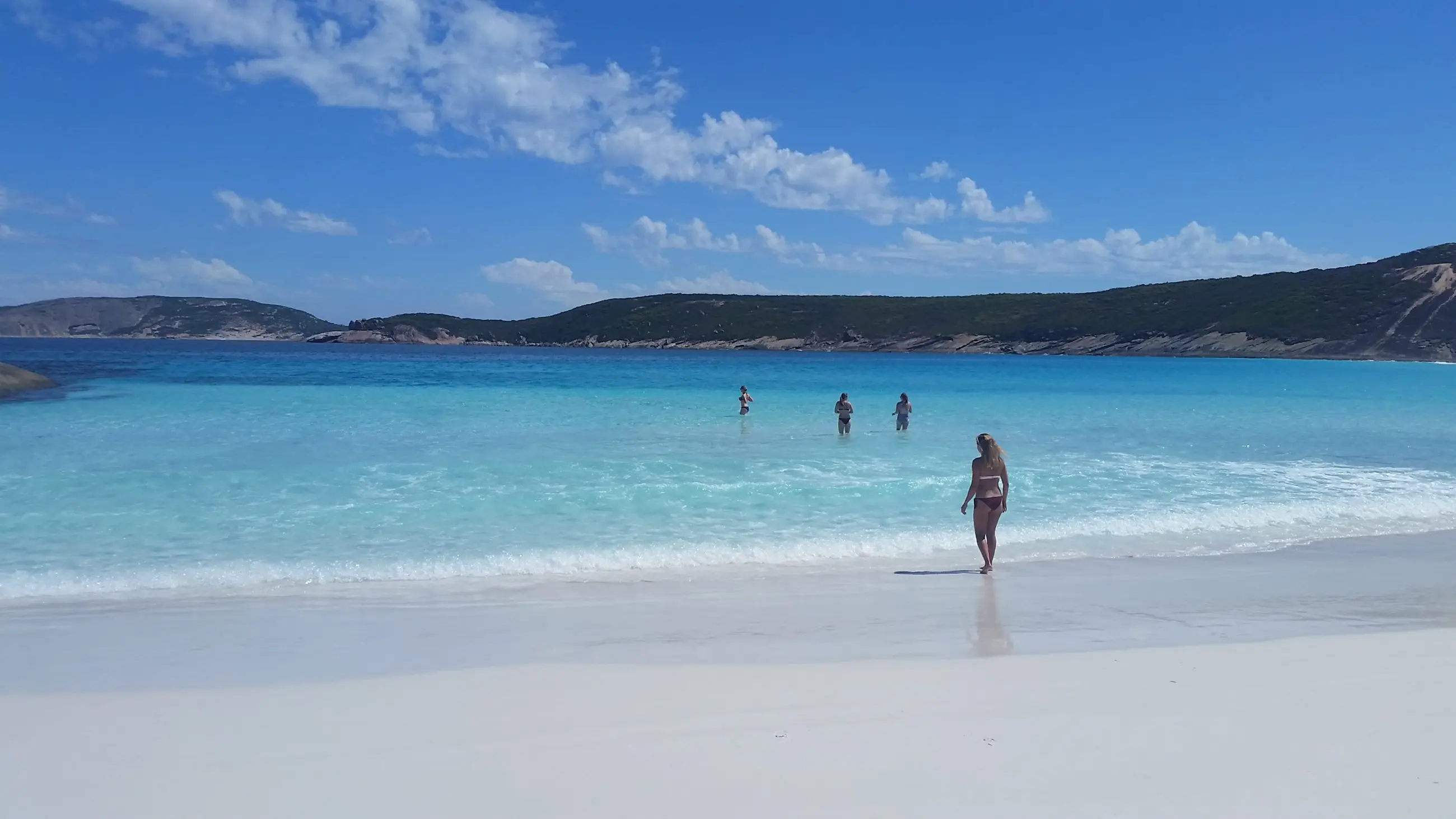 Woman on pristine white sand during 10 Day Perth to Adelaide Adventure Tour by Untamed Escapes; others enjoy crystal-clear blue water.