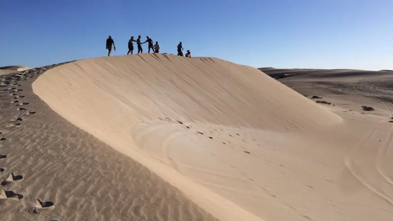 Silhouetted travellers atop golden sand dunes with footprints, enjoying a 10-day Perth to Adelaide Adventure Tour by Untamed Escapes.