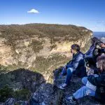 Four travellers relax on a scenic rocky cliff, admiring panoramic Blue Mountains views during a one-day Wildlife Park adventure tour.