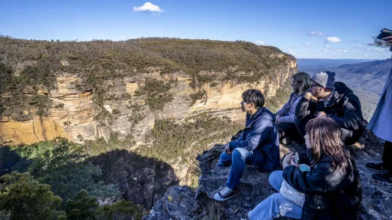 Four travellers relax on a scenic rocky cliff, admiring panoramic Blue Mountains views during a one-day Wildlife Park adventure tour.