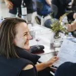 A woman smiles, holding a menu with friends and wine, enjoying a memorable Hunter Valley Signature Wine Tour experience together.