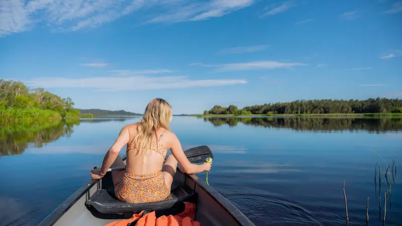 Woman in swimming costume canoeing on tranquil lake during 1 Day Noosa Everglades Explorer Tour, surrounded by scenic natural beauty.