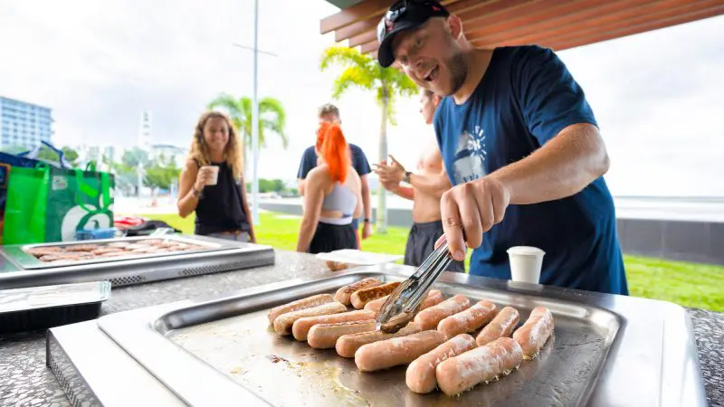 Man expertly grills sausages at lively outdoor BBQ on a 10 Day Oz Intro Sydney to Brisbane group travel adventure for backpackers.