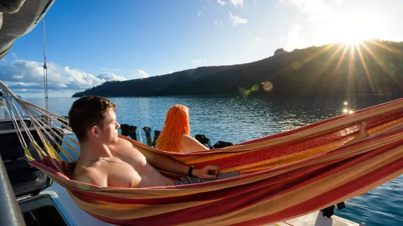 Couple relaxes in a hammock aboard Oz East Coast Adventure boat at sunset, enjoying tranquil water views on 28-day tour of Australia.