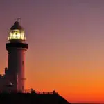 Lighthouse shining at dusk, silhouetted by a colourful sunset during your unforgettable 10 Day Oz Intro Sydney to Brisbane journey.
