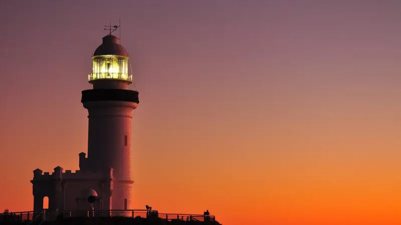 Lighthouse shining at dusk, silhouetted by a colourful sunset during your unforgettable 10 Day Oz Intro Sydney to Brisbane journey.