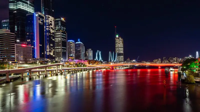 Stunning night city skyline on the 10 Day Oz Intro Sydney to Brisbane route, featuring a glowing red bridge and shimmering river reflections.